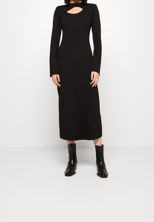 Vestido negro de manga larga con escote en forma de llave, diseño ajustado y largo midi, combinado con botines negros. Textura de tela suave.