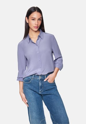 Lavender blouse with a collared neckline, button-up front, and rolled three-quarter sleeves, paired with light blue denim jeans.