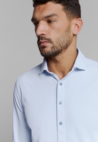 Lichtblauw overhemd met kraag en een gladde textuur, met een knoopsluiting aan de voorkant en contrasterende blauwe knopen, een slim-fit met lange mouwen.