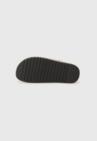 Zool van een schoen met een geribbelde zwarte rubberen oppervlakte en een lichtbruine tussenzool, die grip en stabiliteit biedt met gestructureerde details.