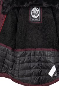 Chaqueta de piel sintética forrada de pelo negro con una sección inferior acolchada en negro, acentos rojos y una etiqueta de tamaño que presenta un logo decorativo en su interior.