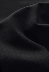 Black fabric with a smooth, textured surface, displays gentle folds and undulations, highlighting its soft, flexible quality.