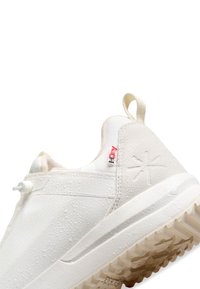 Zapatilla deportiva blanca con una suela de goma texturizada, parte superior impermeable y un diseño minimalista. Presenta una pequeña etiqueta roja y gotas de agua.