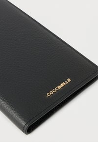 Portafoglio in pelle nera con finitura texturizzata. Presenta un logo dorato impresso sulla parte anteriore. Design pulito e rettangolare con bordi arrotondati.