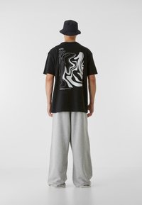 Black t-shirt with abstract white design on the back, paired with loose-fitting gray sweatpants, and a black bucket hat.