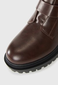 Pruun nahast pahkluu saabas ümarate varvastega, millel on Velcro rihm ja tekstureeritud must kummist talla, mis tagab haarde ja vastupidavuse.