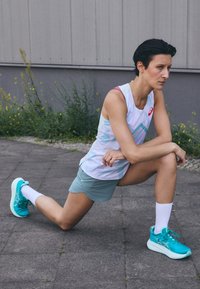 Athletic tank top in light pastel colors and geometric patterns, paired with green shorts and teal running shoes; white crew socks visible.