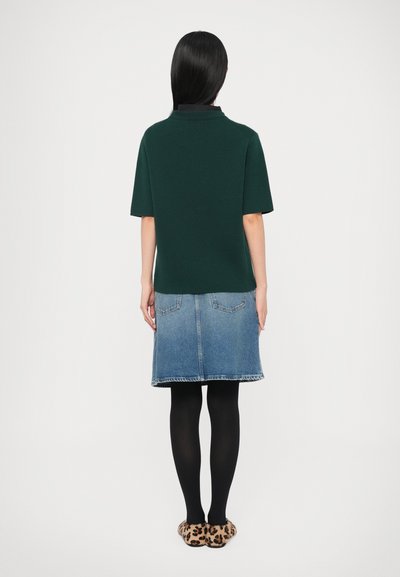 Zaļš īsroku džemperis ar polo apkakli, kombinēts ar zilu džinsa svārku, melnām zeķbiksēm un leopardā rakstāma čībām.