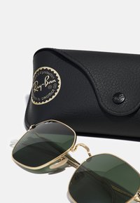 Ochelari de soare Ray-Ban cu lentile verzi, ramă din metal auriu și etui texturat negru cu un logo auriu și închidere tip snap.