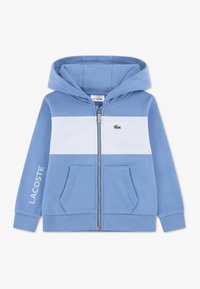 Μπλε φούτερ με φερμουάρ, με λευκή οριζόντια ρίγα, εμπρόσθιες τσέπες, ραβδωτά μανσέτες και μικρό πράσινο λογότυπο Lacoste στο στήθος.