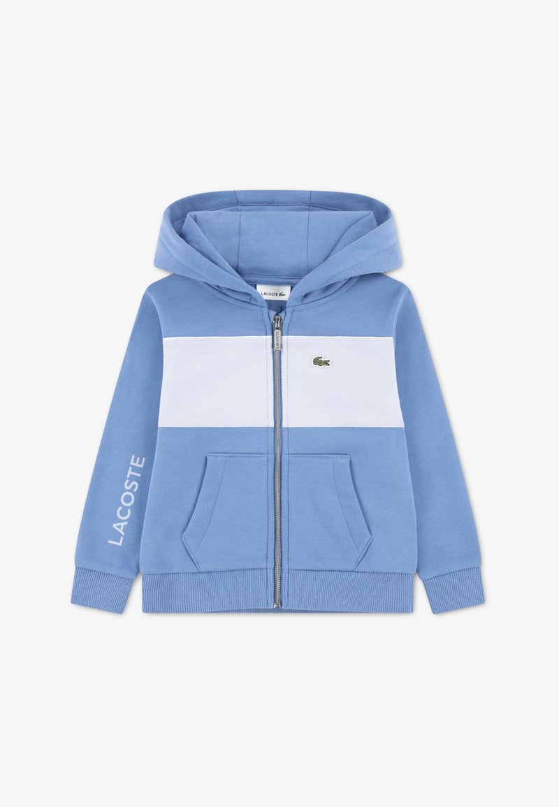 Modrá mikina na zip s bílým vodorovným pruhem, předními kapsami, žebrovanými manžetami a malým zeleným logem Lacoste na hrudi.