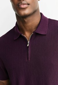 Fialová rebrovaná polo košeľa s krátkym zipsom a plochým golierom, s textúrovanou tkaninou a jemným leskom.
