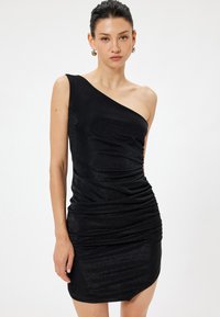Schwarzes, einseitig tragbares Kleid aus glänzendem, dehnbarem Stoff mit gerafften Details und asymmetrischem Saum. Glatte Textur mit leichtem Schimmer.