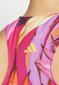 Débardeur de sport coloré avec un design rose vibrant, des motifs abstraits, un logo jaune et des détails de couture minimalistes.