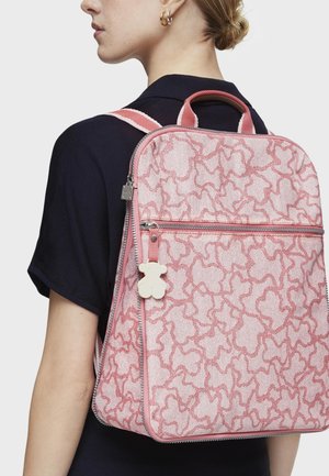 Sac à dos rose à motifs avec une surface texturée, doté d'une fermeture éclair contrastante, d'un petit charme en forme d'ourson en peluche et de bretelles doubles.