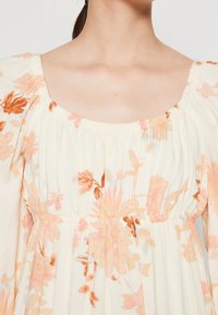 Kwiatowa sukienka z kwadratowym dekoltem, bufkami, marszczonym pasem oraz miękkim, lekkim materiałem w kremowych, pomarańczowych i pastelowych odcieniach.
