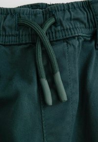 Ciemnozielone szorty z materiału z elastycznym paskiem w taliach i sznurkiem, który ma teksturowane, gumowane końce. Gładki, trwały materiał.