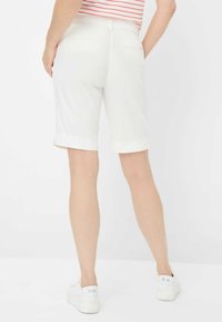 Weiße Baumwollshorts mit umgeschlagenem Saum und Gesäßtaschen. Von hinten gezeigt, kombiniert mit weißen Sneakers und einem gestreiften Oberteil.