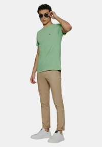 T-shirt en coton vert à manches courtes, chinos beiges et baskets blanches. Le t-shirt présente un petit logo sur la poitrine.