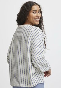 Maglione lavorato a maglia color crema con strisce orizzontali blu, caratterizzato da una vestibilità morbida, maniche ampie e scollo rotondo. Dettaglio in tessuto testurizzato.