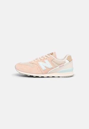 Baskets New Balance rose clair et beige avec logo "N" blanc, tige en mesh et en suède, et détail bleu clair sur le talon de la semelle.