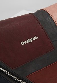 Vícebarevná kožená taška s tmavě červenými, černými a broskvovými sekcemi. Obsahuje stříbrné logo "Desigual" a stříbrný zip.