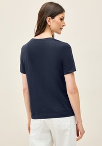 T-shirt bleu marine à manches courtes avec un col rond et une coupe décontractée, fabriqué à partir d'un tissu doux, associé avec un pantalon blanc.