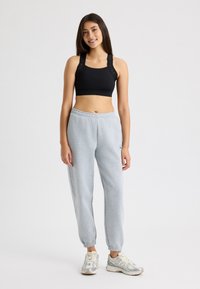 Sujeción negra con tirantes anchos y detalle del logo combinada con pantalones de chándal grises claros que cuentan con una cintura elástica y puños en los tobillos.