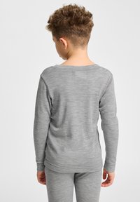 Graues Langarmshirt aus weichem, strukturiertem Stoff, mit einem breiten Rundhalsausschnitt und einer lockeren Passform, kombiniert mit passenden grauen Hosen.