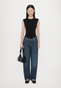 Melna bezpiedurkņu bodijs, augsta jostasvieta zili džinsi, melna studēta rokassoma, melni slip-on apavi ar akcentiem, minimālisma dizains.