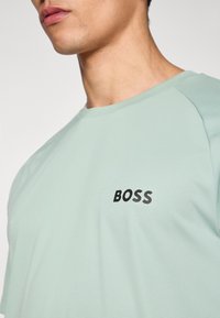 Licht muntgroen overhemd met korte mouwen en geribbelde halslijn. Voorzien van het "BOSS"-logo in zwart aan de linkerkant, met een gladde textuur en subtiele strepen.