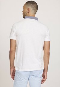 Polo shirt blanc à manches courtes avec un col en chambray bleu. Le matériau semble léger, avec une texture lisse et sans motifs visibles.