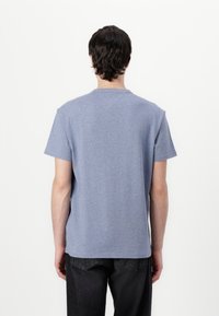 T-shirt κοντομάνικο, με στρο�γγυλή λαιμόκοψη σε ανοιχτό μπλε ύφασμα με μαλακή υφή. Χαλαρή εφαρμογή, εμφανίζεται από πίσω, συνδυασμένο με σκούρα τζιν.