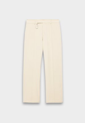 Pantalons beige à jambes larges avec un devant plat, des passants de ceinture et un détail en clip métallique sur la taille. Texture lisse et design ajusté.
