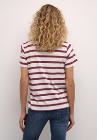 Stripet t-shirt i beige med maroon vandrette striber, korte ærmer og rund kant. Bæres med blå jeans. Textureret, afslappet pasform.