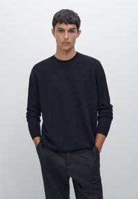Marineblaues Sweatshirt mit Rundhalsausschnitt, langen Ärmeln und gerippten Bündchen, kombiniert mit grauen Hosen. Glatte Textur und minimales Design.