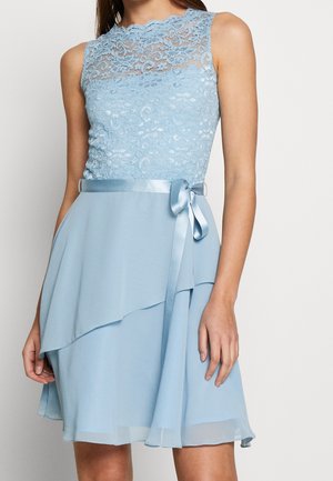 Bezrekawnikowa, jasnoniebieska sukienka z koronkowym górnym częścią, satynową wstążką w pasie zawiązaną na kokardę oraz warstwową, asymetryczną spódnicą.