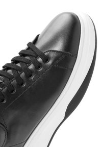 Sneaker in pelle nera con lacci neri e una suola in gomma spessa bianca e nera, mostrata in primo piano dall'alto.