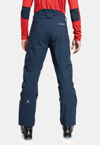 Marineblaue Skihosen mit einer schlanken Passform, hoher Taille, verstärkten Nähten und einem Logo auf der Rückseite. Das Material wirkt glatt und strapazierfähig.