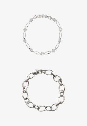 Két ezüst karkötő: az egyik ovális szemekből áll, kör alakú kristálykövekkel díszítve, a másik nagyobb, texturált ovális szemeket tartalmaz, és kapcsolókapoccsal van ellátva.