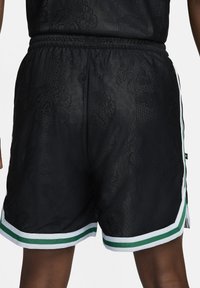 Bermudas deportivas de malla negra con un sutil patrón texturizado, que presentan acentos en verde y blanco a lo largo del dobladillo y la cinturilla.