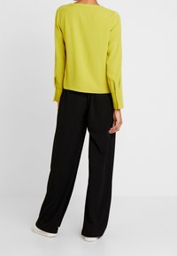 Lime vihreä paita pitkillä hihoilla ja nappikiinnityksellä, yhdistettynä mustiin leveälahkeisiin housuihin. Liukas kangas ja rento istuvuus.