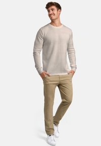 Világosszürke kötött pulóver texturált vízszintes csíkokkal, bézs chino nadrággal és fehér sportcipővel párosítva. A modell zsebre tett kézzel áll.