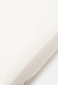 Calvin Kleinin valkoinen nahkalaukku, jossa on sileä pinta ja kohopainettu logo. Suorakaiteen muotoinen, puhdas ja minimalistinen muotoilu.