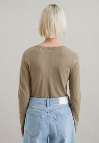 Long-sleeve olive green top with a crew neck, paired with light blue high-waisted jeans featuring a white label and back pockets.
