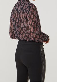 Blusa negra transparente con patrón de hojas rosas, de mangas largas y con escote fruncido, combinada con pantalones ajustados negros con acentos de tachuelas en los laterales.