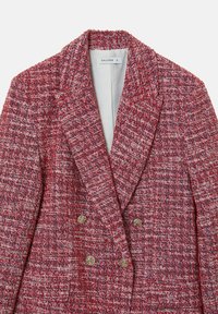 Blazer in tweed rosso e bianco con finitura texturizzata, caratterizzato da una chiusura doppiopetto e due bottoni dorati nella parte inferiore.