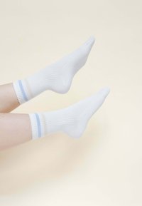 Weiße gerippte Socken mit blauen und beigen Streifen am Bündchen, mit glatter Textur und schlichter Gestaltung, auf einem neutralen Hintergrund präsentiert.