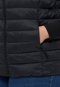 Juodas paminkštintas liemenė su horizontaliu siuvimu. Yra užtrauktuko uždarymas ir šoninės kišenės, pagaminta iš lygaus, lengvo audinio.