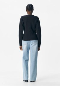 Svart stickad tröja med långa ärmar, lätt avsmalnande midja, kombinerad med ljusblå raka jeans, bärs med svarta skor.